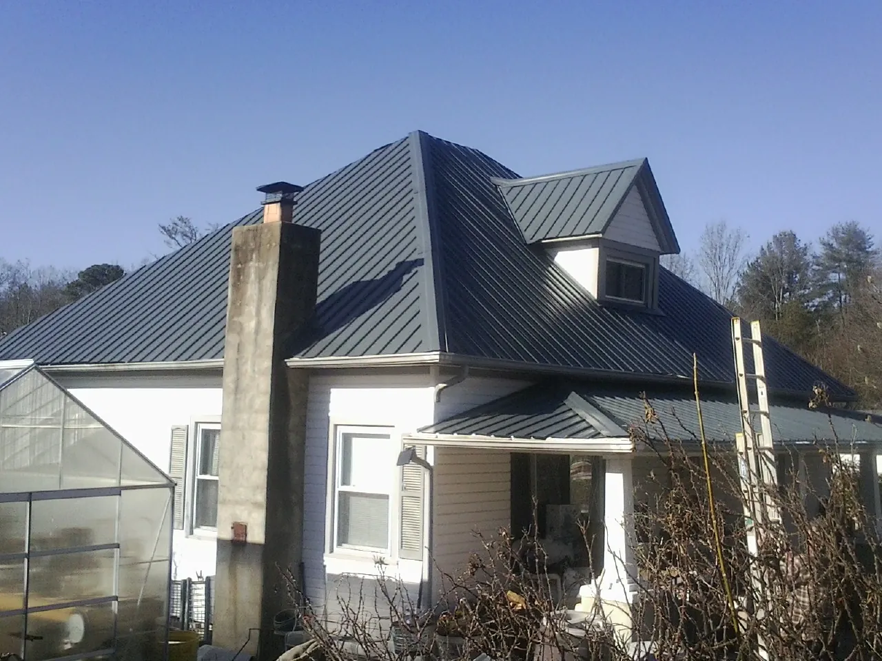 Dark blue standing seam metal roof on a white farmhouse with dormer — Slate & Tile Roof Repair by Roofing Brothers in Cutchogue