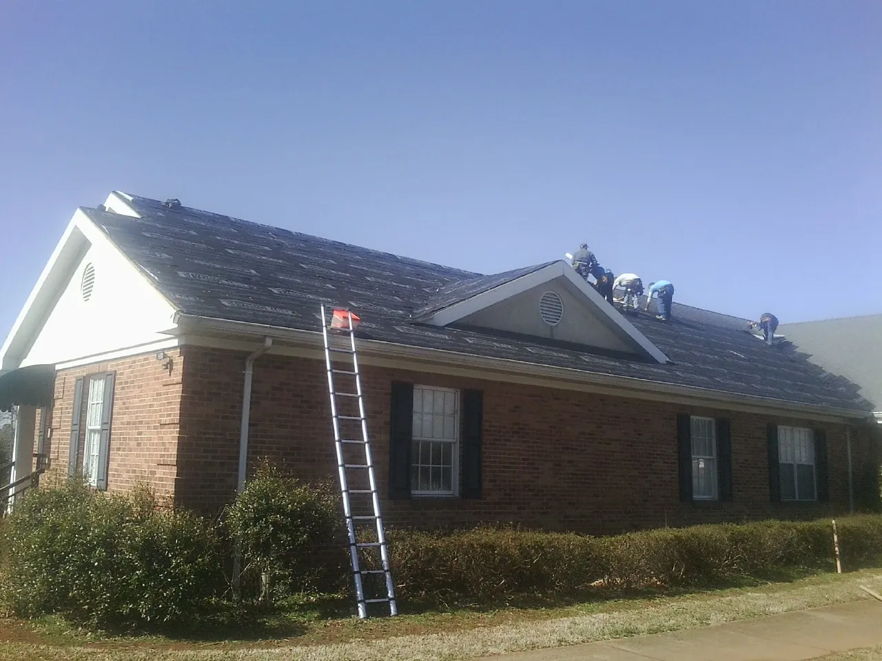 Crew tearing shingles off a brick ranch roof with a ladder set in Cutchogue