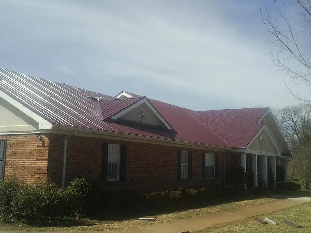 Red metal roof with gabled entries on a long brick building, from a Hail Damage Roof Repair job in Cutchogue