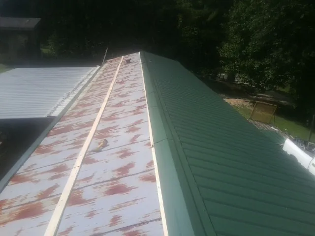 Old rusted panels beside newly installed green metal roofing — Wind Damage Roof Repair by Roofing Brothers in Cutchogue