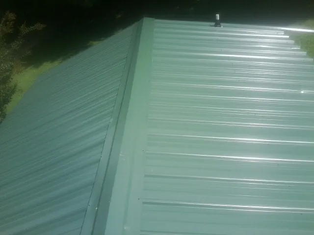 New green metal panels meeting at the ridge of a roof — Flat Roof Repair work by our crew in Cutchogue