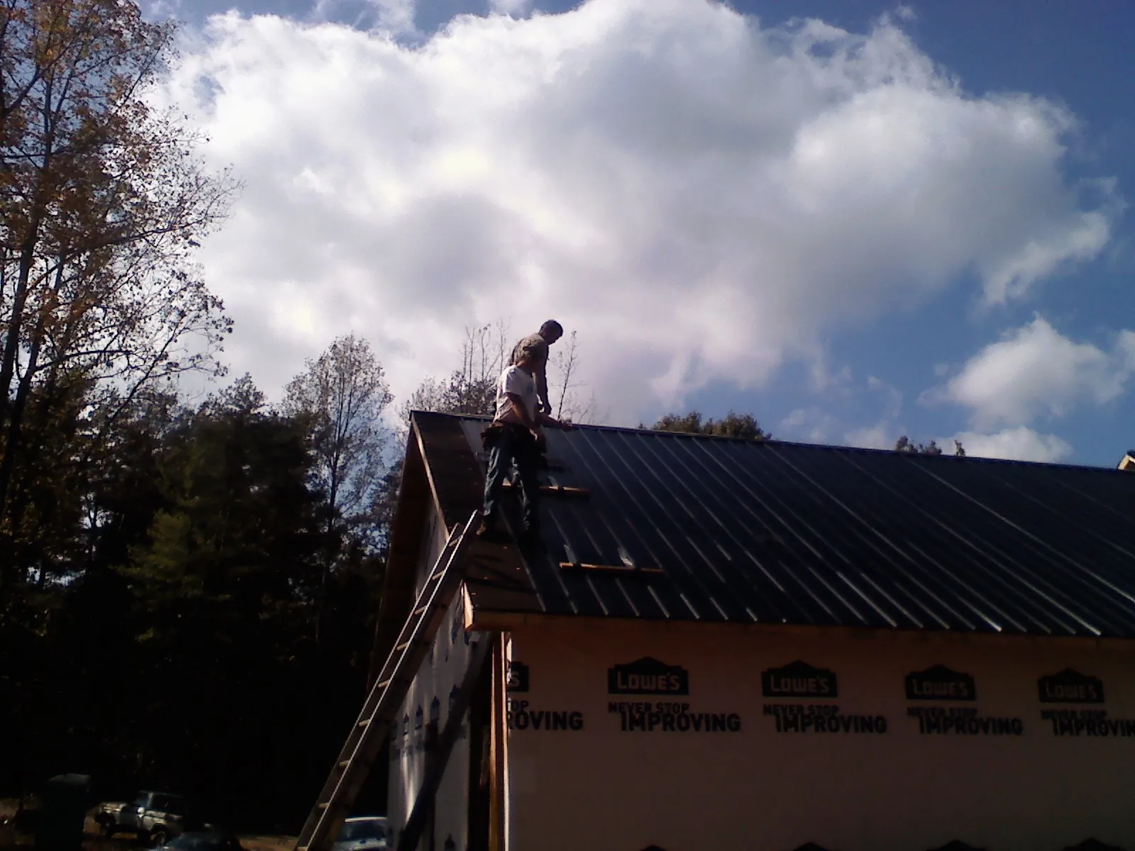 Roofer fastening dark metal panels high against a cloudy sky, from a Roof Inspection job in Cutchogue