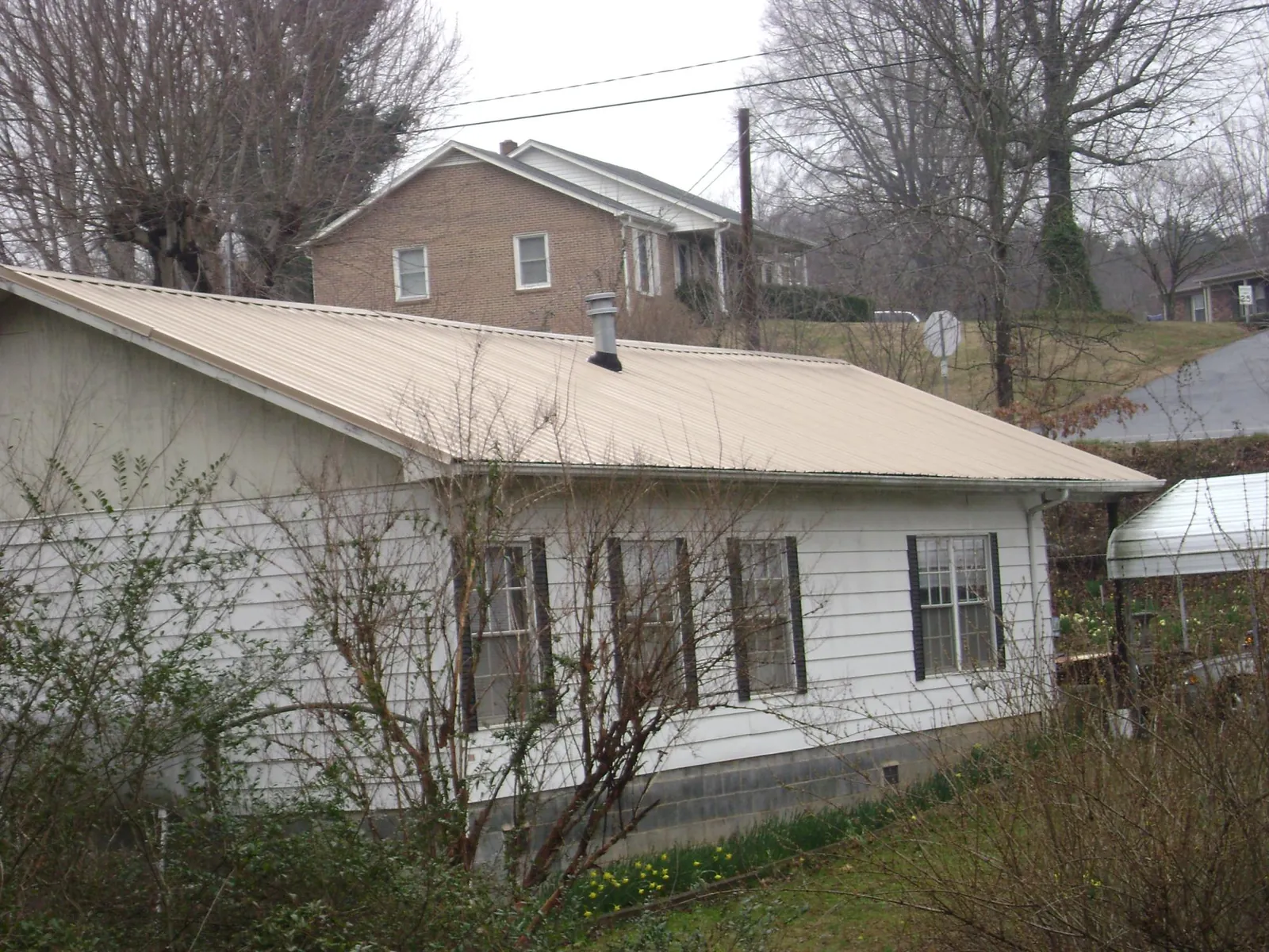 Tan metal roof on a white sided house set into a hillside — Commercial Roofing by Roofing Brothers in Cutchogue
